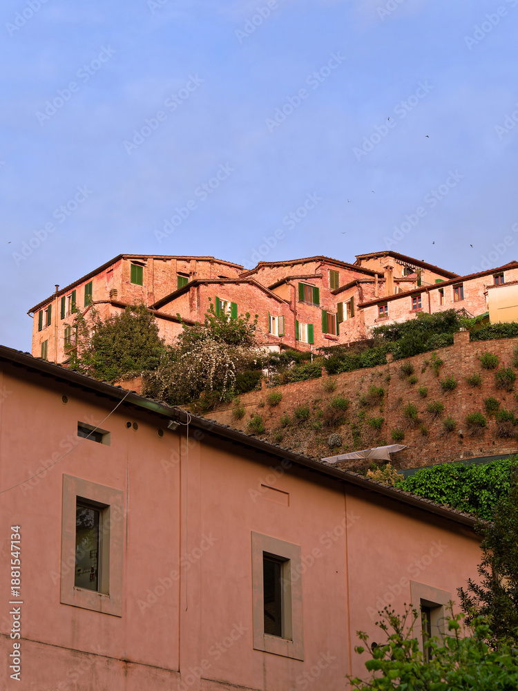 Fototapeta premium Old houses perch on a scenic cliff near Siena’s historic center, blending into the Tuscan landscape. A cultural travel in Italy.