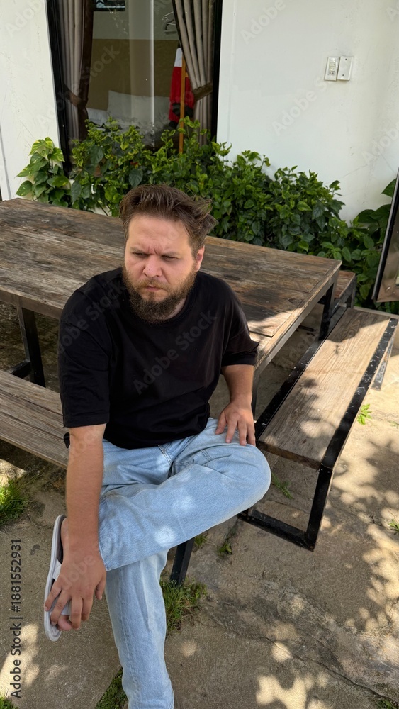 Fototapeta premium Pensive Man with Furrowed Brow Sitting at Outdoor Table, Deep in Thought