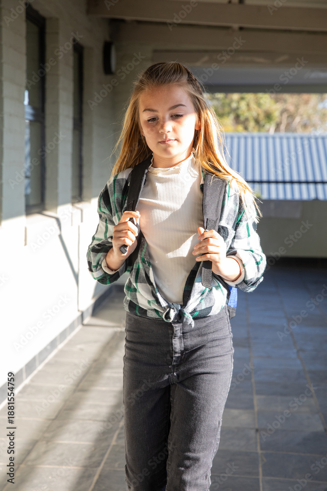 Obraz premium School-age girl walking through tiled school corridor with backpack straps under bright sunlight