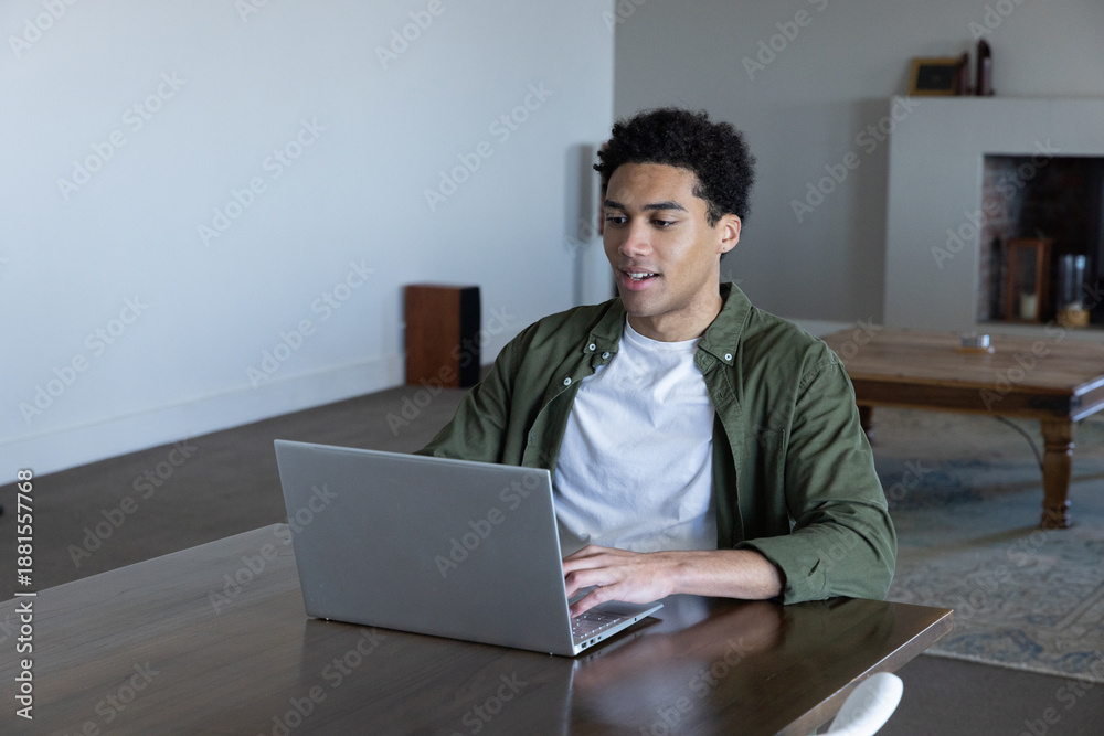 Fototapeta premium African american man sitting at dining table in living room working on laptop
