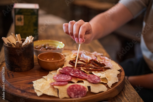 Fotografie Close-up of a person picking cured meats with a toothpick from a traditional Ita