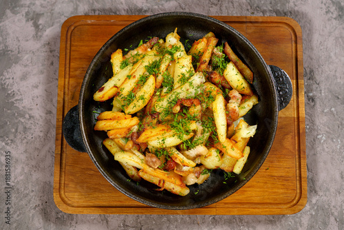 Crispy fried potatoes topped with herbs and savory meat served in a skillet on wooden cutting board