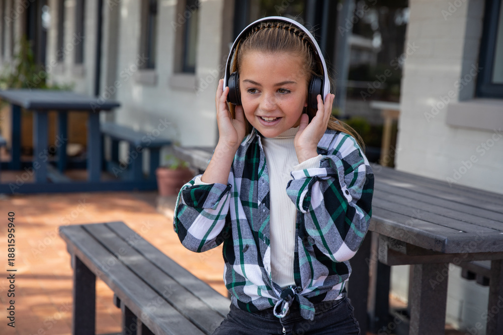 Obraz premium Girl child with over-ear headphones against head on brick patio under porch with picnic tables