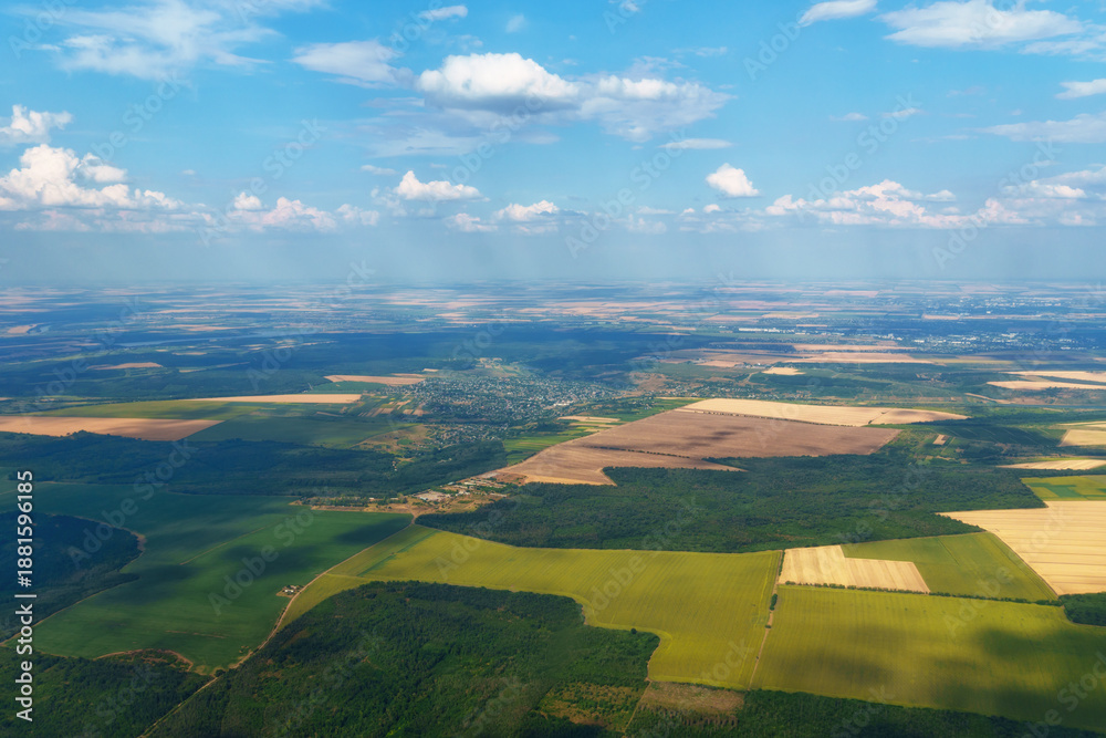 Obraz premium Aerial view of vast green plains and small villages taken from airplane window during summer flight