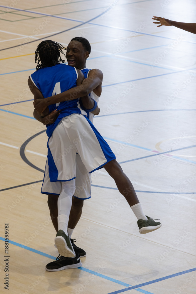 Obraz premium Basketball players in blue uniforms celebrating after scoring on polished wooden court