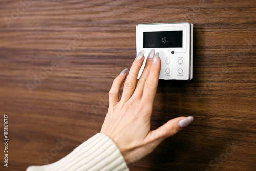 Foto Hand adjusting a digital thermostat on a wooden wall, displaying temperature set
