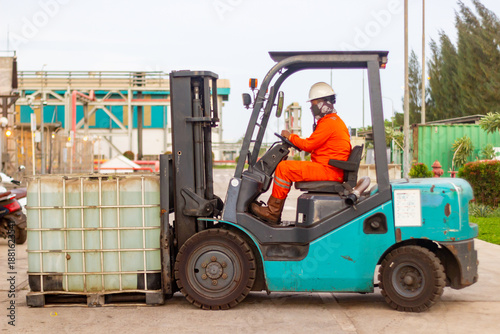 Industrial Worker in Protective Gear Operating a Forklift to Transport Large Liquid Containers in a Manufacturing Facility
