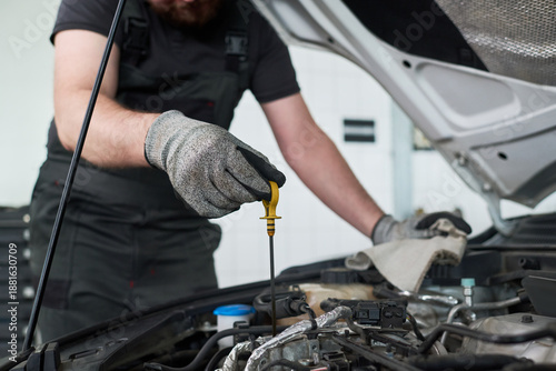Foto Midsection of man checking oil level in car engine bay, wearing work gloves and