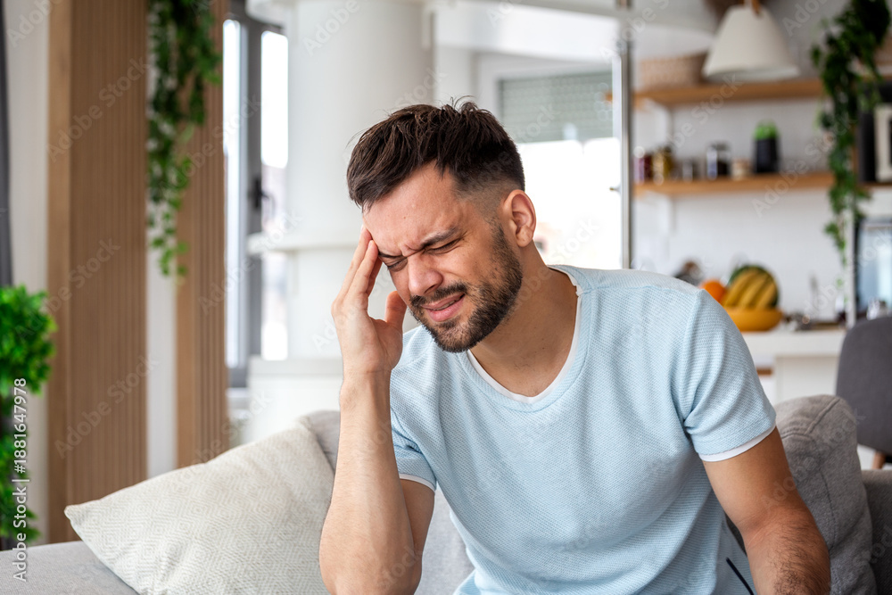 © Graphicroyalty - Young man holding his head in pain while suffering from a severe headache or migraine at home caused by stress or tension and high blood pressure while feeling fatigue and exhaustion © Graphicroyalty - Young man holding his head in pain while suffering from a severe headache or migraine at home caused by stress or tension and high blood pressure while feeling fatigue and exhaustion