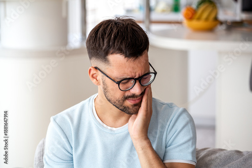 Tableau sur toile Young man in glasses suffering from severe toothache and jaw pain at home; concept for dental emergency, sensitive teeth, cavity, oral health, and need for professional dental care