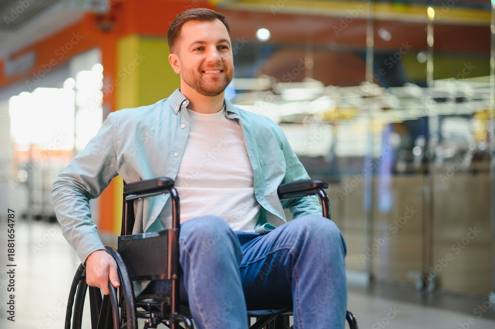 Obraz premium Smiling man using wheelchair moving in shopping mall corridor