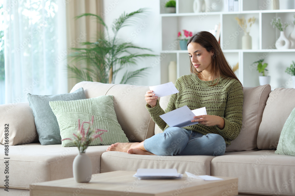 Fototapeta premium Serious woman in green reading a paper letter at home