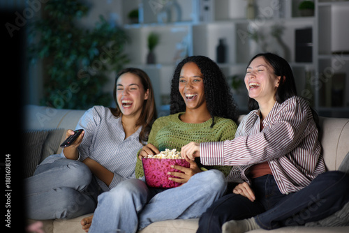 Bild auf Leinwand Happy diverse friends eating popcorn watching tv in the night