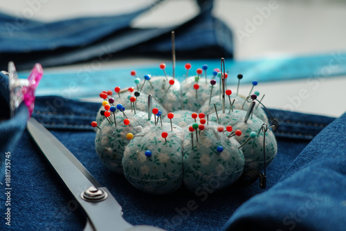 Close-up of a pincushion filled with colorful sewing pins on blue denim fabric. Sewing, tailoring and handmade craft concept.