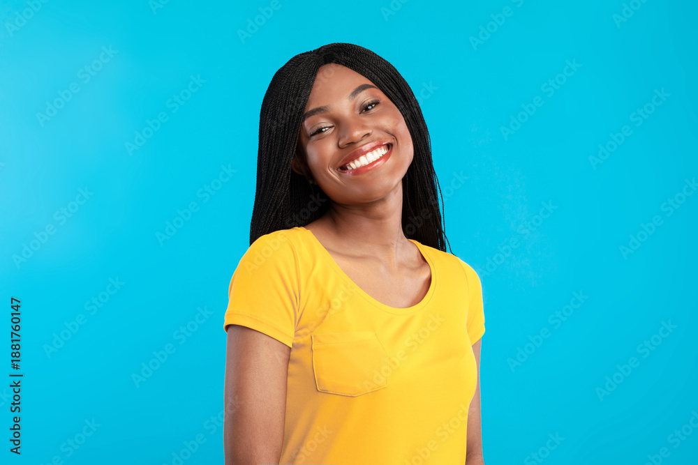 Fototapeta premium Cheerful Black Woman With Braided Cornrows Hairstyle Smiling To Camera Posing Standing Over Blue Background. Studio Portrait Of Pretty African American Young Lady With Toothy Smile Concept