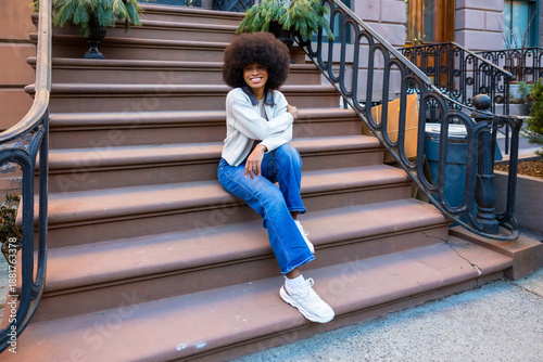 Tablou pe pânză Smiling woman sitting on brownstone stoop enjoying city life