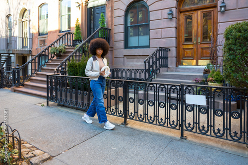 Young woman walking city street with brownstone buildings