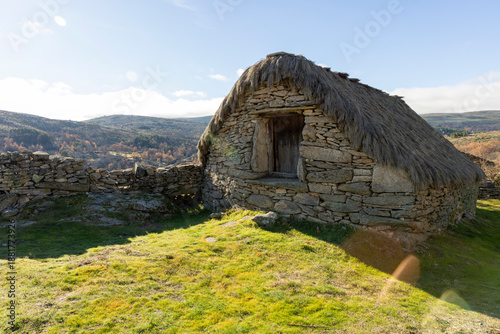Fotografie A small, weathered stone building with a thatched roof sits on a grassy hillside