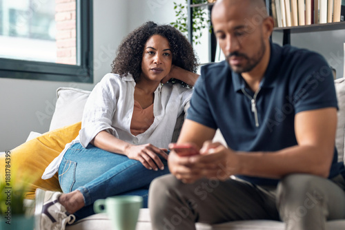 Photos Angry couple sitting on couch together and looking to opposite sides while using smartphone at home