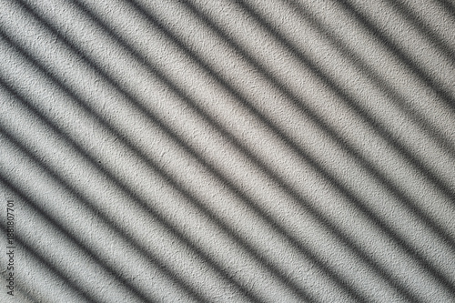 Rough cement wall in grey color covered by shadow in stripped lines from the sunlight through the window.
