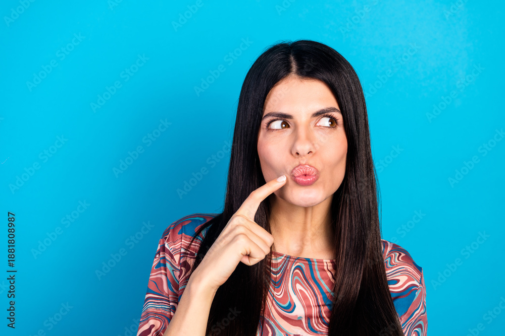 Fototapeta premium Young woman in a stylish patterned shirt poses playfully against a blue background for fashion lifestyle advertising and stock photo use