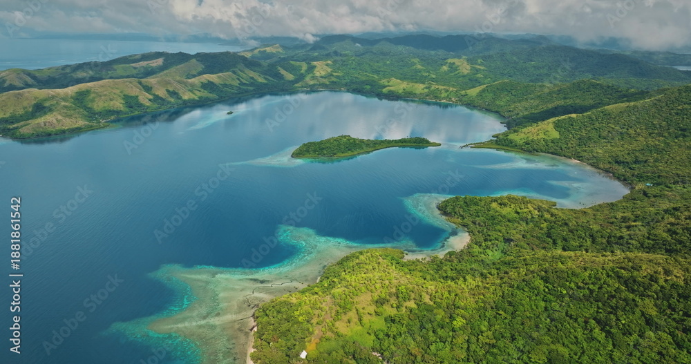 Obraz premium Islands covered with lush green rainforests surrounding a tranquil turquoise bay, featuring shallow coral reefs reflecting clear waters and an overcast sky