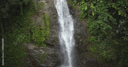 Fiji, Nadi Waterfall: Crystal clear water cascading down a moss covered cliff, surrounded by lush greenery, creates a breathtaking rainforest scene. Wild nature landscape. Drone flight zoom in