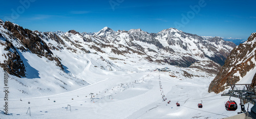 Fotografia Stubai glacier in Austrian Alps with ski slopes, cable car gondola lift, chairlift with skiers and snowboarders and a ski tow