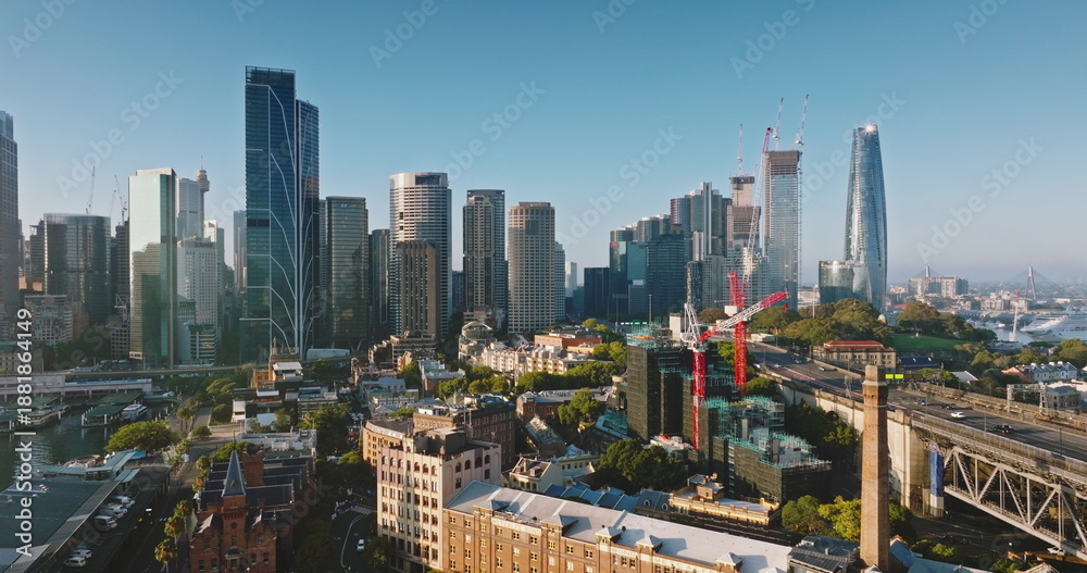 Fototapeta premium Australia, Sydney: Sydney's cityscape aerial view with tall skyscrapers buildings, construction cranes, streets, traffic road, bridge and modern architecture in morning light. Drone flight panorama
