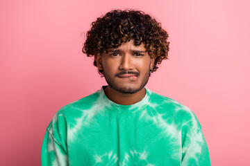 Young man with curly hair wearing green tie dye sweatshirt posing against pink background