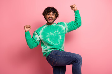 Happy man in green tie dye sweater celebrating joy and energy against pink background studio backdrop