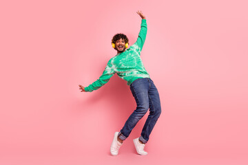 Happy young man dancing in a pink studio wearing a green tie dye sweater jeans and white sneakers with headphones