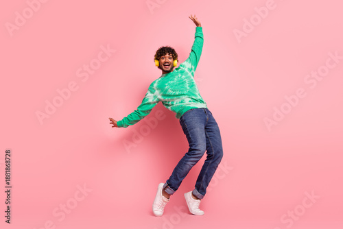 Slika na platnu Happy young man dancing in a pink studio wearing a green tie dye sweater jeans a