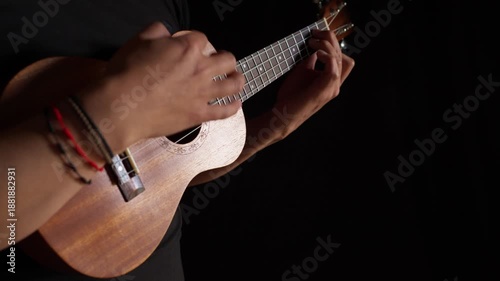 Hands playing a classic brown acoustic ukulele with white wooden strings on a black background as a folk musical instrument ready to play a jazz and rock concert.