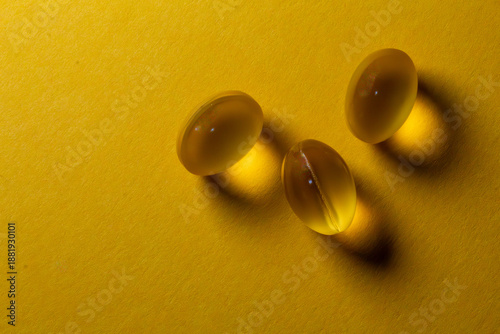 Minimalist composition of three yellow gel capsules on a bright yellow background, vitamin D or omega-3 supplement concept.