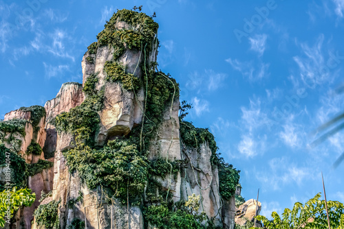 A mountain covered in green plants and trees. The sky is blue and clear. The mountain is very tall and has a lot of vegetation growing on it