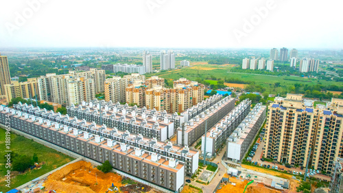 aerial drone shot symmetrically placed flats, houses, with skyscrapers at the back showing mass produced modular homes growing the real estate segment
