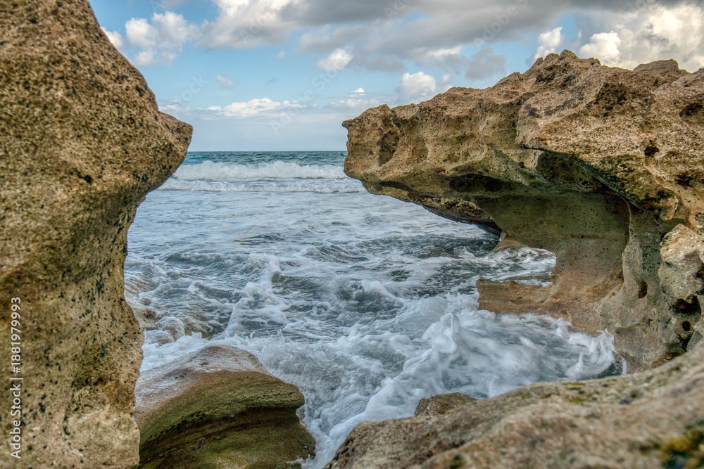 Fototapeta premium The ocean is rough and the rocks are jagged. The waves are crashing against the rocks, creating a powerful and dynamic scene. The water is a deep blue color, and the sky is a clear blue color