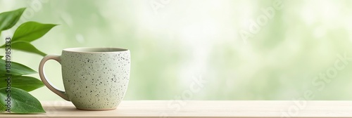 Speckled ceramic mug on wooden table with green leaves. Soft nature bokeh background with copy space. Morning tea or coffee concept