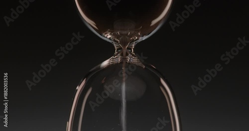 Closeup of hourglass measuring time over a dark dramatic background. Macro view of sand falling down inside the glass clock counting minutes. Concept of time and life flowing.