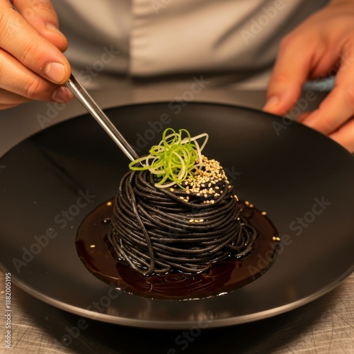 Chef garnishing black squid ink pasta with sesame seeds and scallions on dark plate