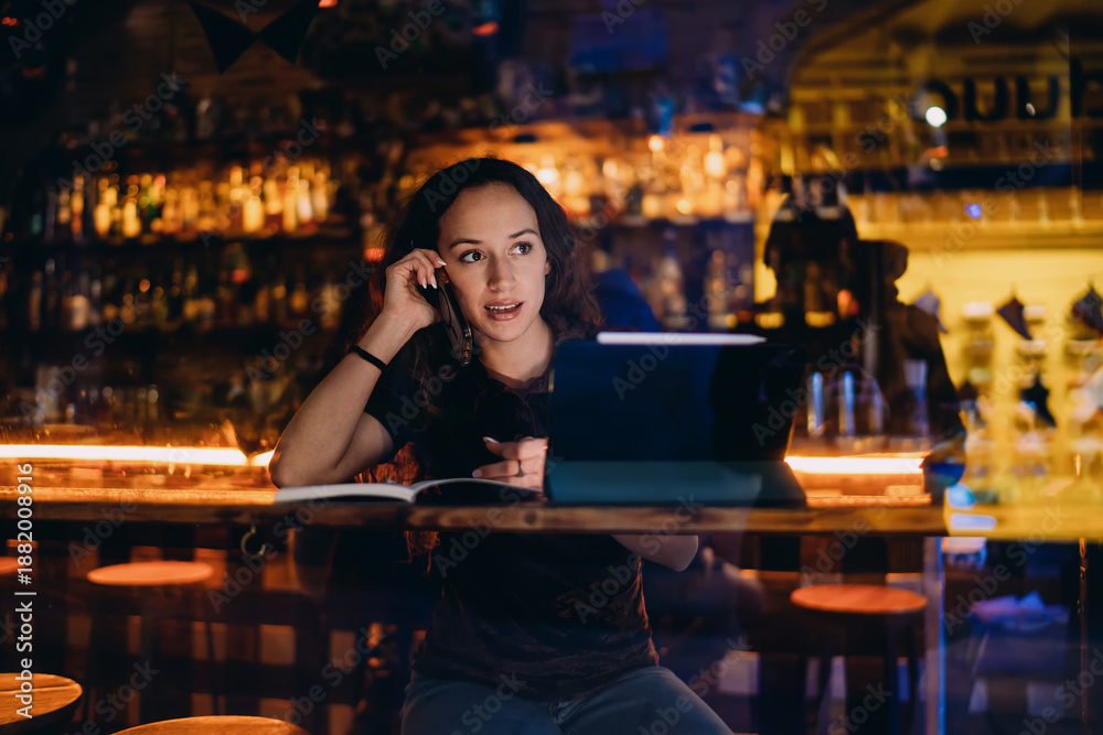 Fototapeta premium Freelancer woman working in bar with notebook, tablet and smartphone — embodying remote flexibility and full digital immersion in a modern multitasking setting.