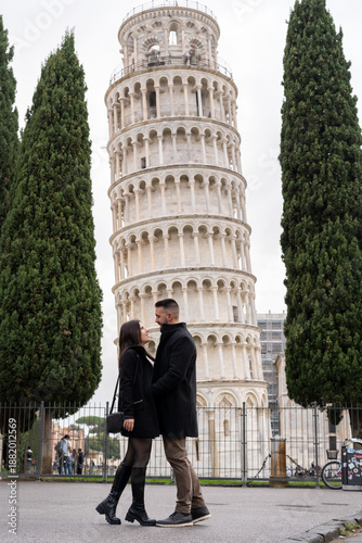 young couple walking together near the famous Leaning Tower of Pisa in Italy on a cloudy day. They are enjoying a sightseeing walk in one of Europe’s most iconic travel destinations.