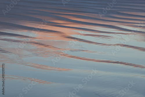 Evening sky reflection in shiny surface of rippling beach sand