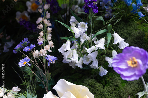 A lush arrangement of white bell shaped flowers and purple blossoms hang gracefully among deep green moss.