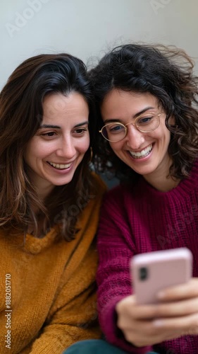 Two joyful friends share a moment of laughter over their phone.