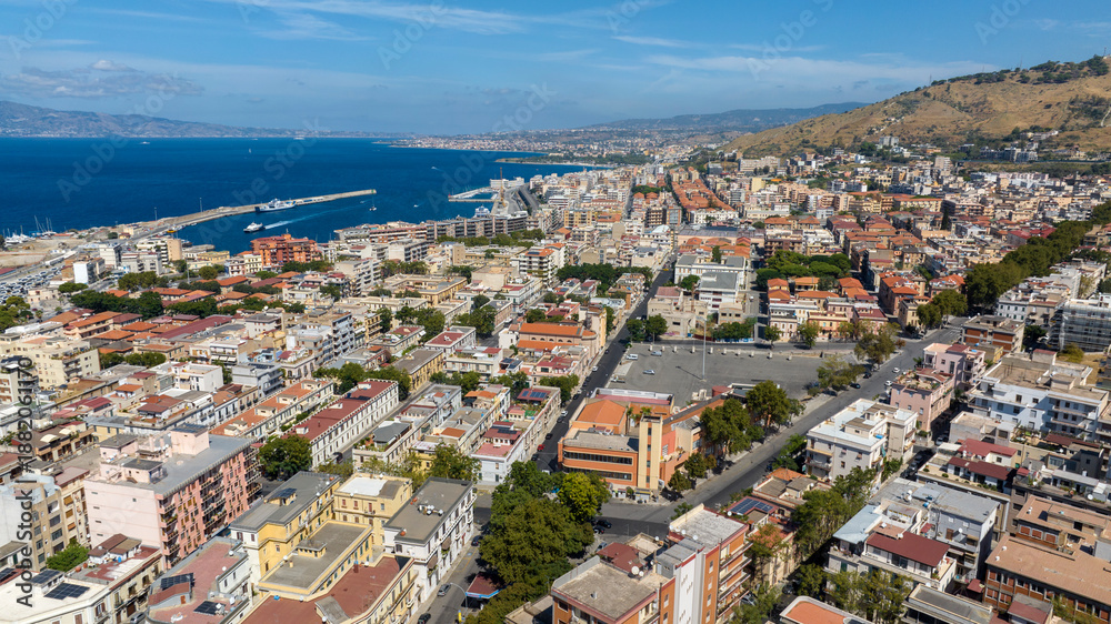 Obraz premium Aerial view of the outskirts of the city of Reggio Calabria, Italy. In the background is the city port, and beyond the Strait of Messina, Sicily can be seen, separated by the sea.