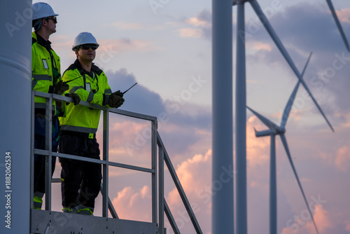 Two wind turbine engineers inspect farm windmills during early evening in the United States