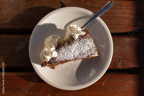 fetta di torta al cioccolato in primo piano come dessert, su un piatto bianco, vista da sopra, con panna, su un tavolo di legno color marrone scuro, di giorno, a pranzo