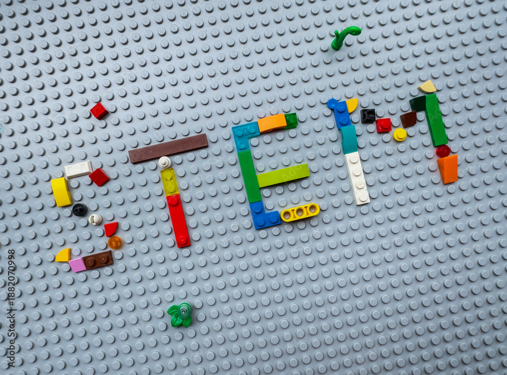 Naklejka premium Word STEM made of colorful plastic LEGO bricks on a gray baseplate, representing science and technology education concept: 25.05.2024- Ljubljana, Slovenia